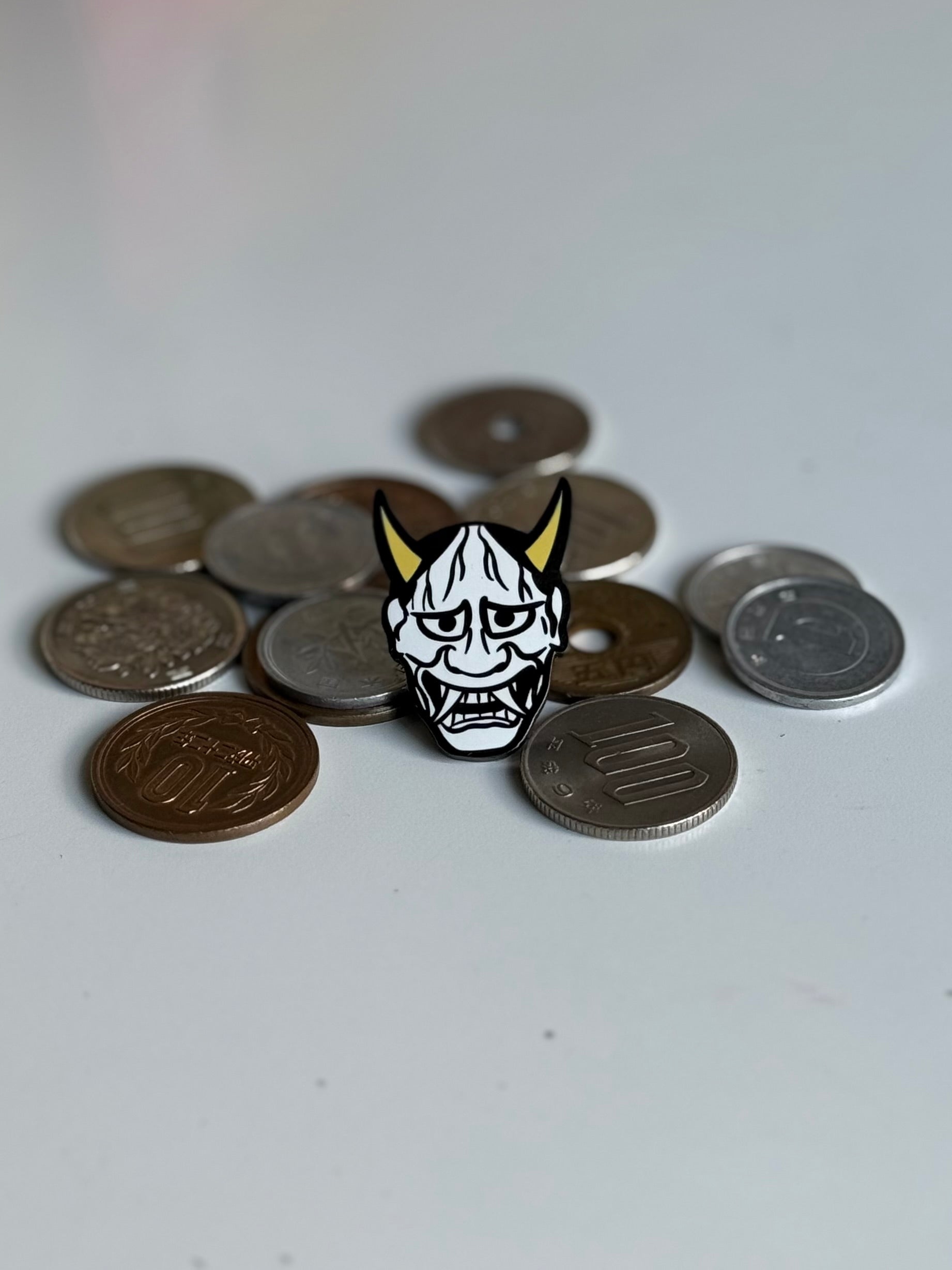 Japanese Hannya enamel pin displayed on Japanese yen coins