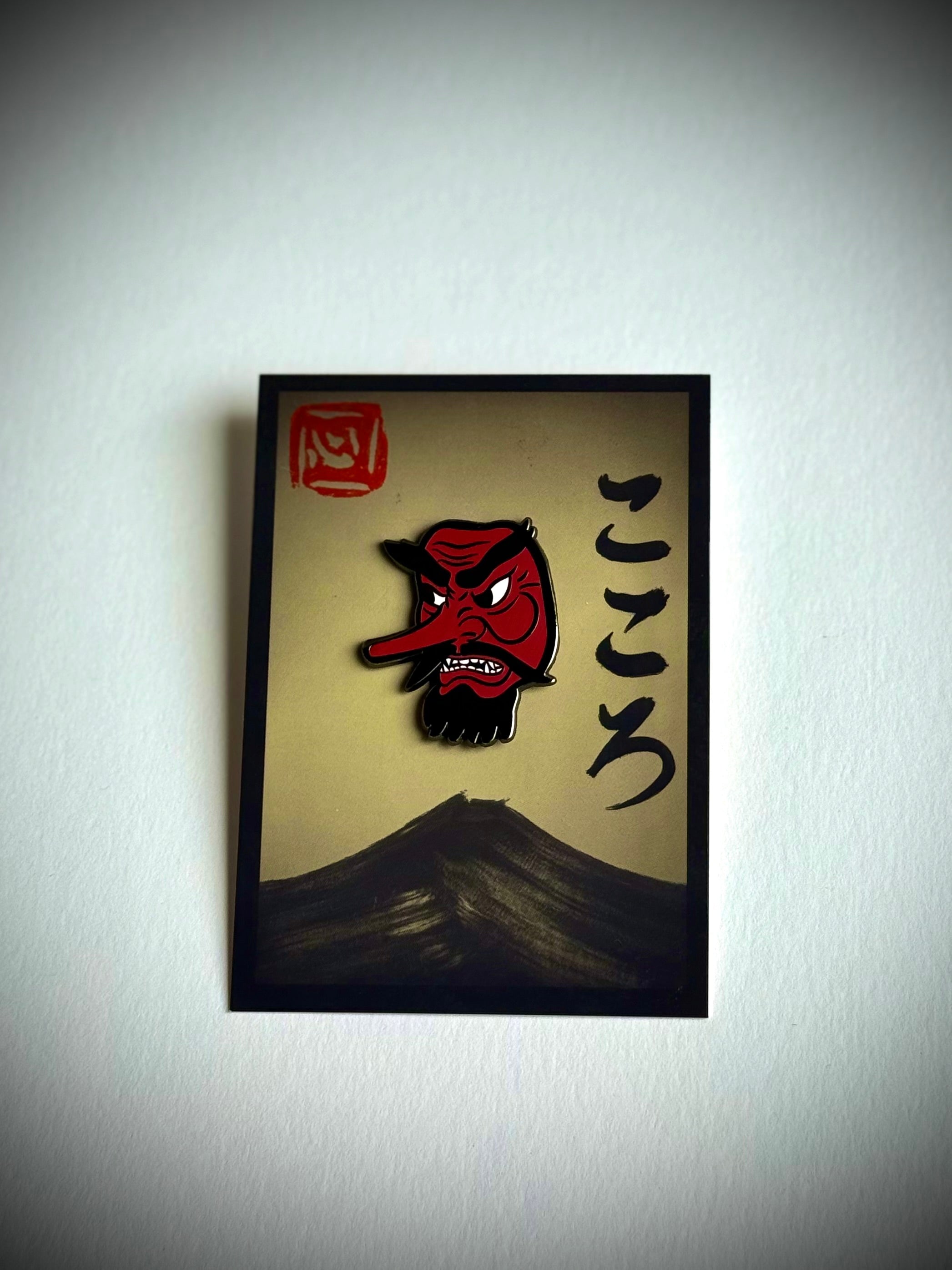 Tengu enamel pin on cream Kokoro backing card with hanko stamp.
