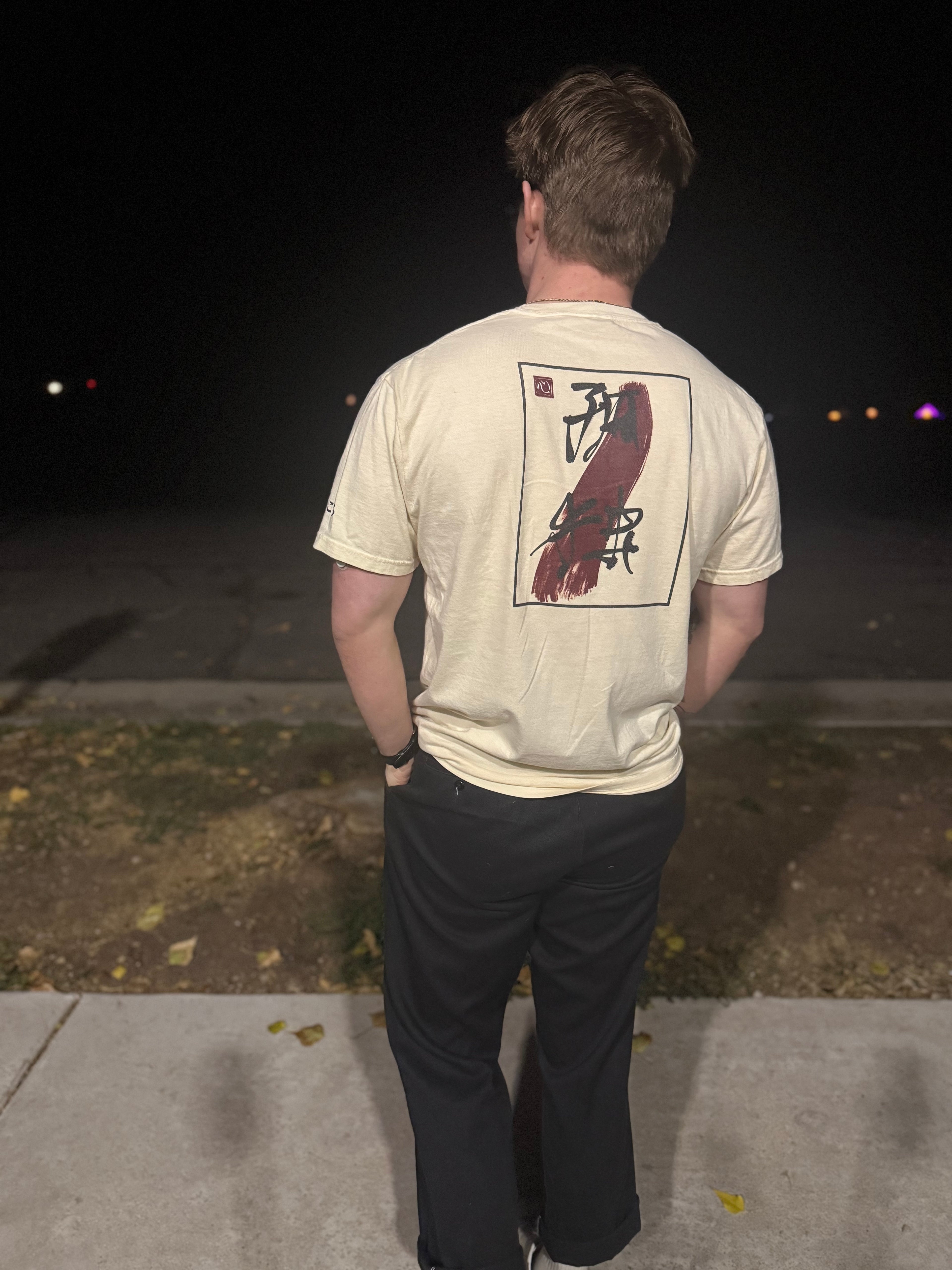 Person wearing cream tee with “isolation” written in black Japanese calligraphy over a red brush stroke graphic at night