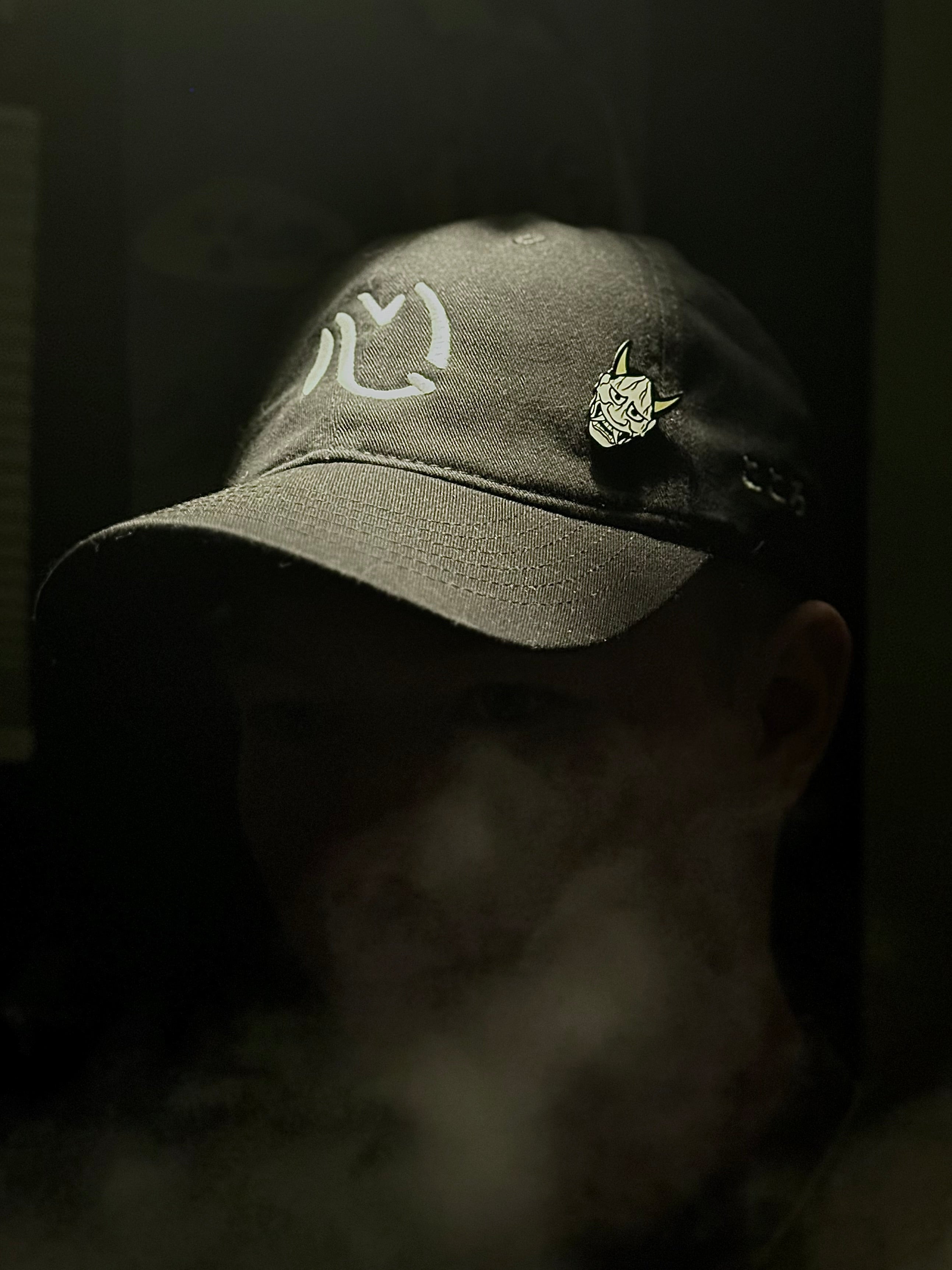 Person wearing black Kokoro dad hat with Japanese embroidery and a hannya mask enamel pin attached