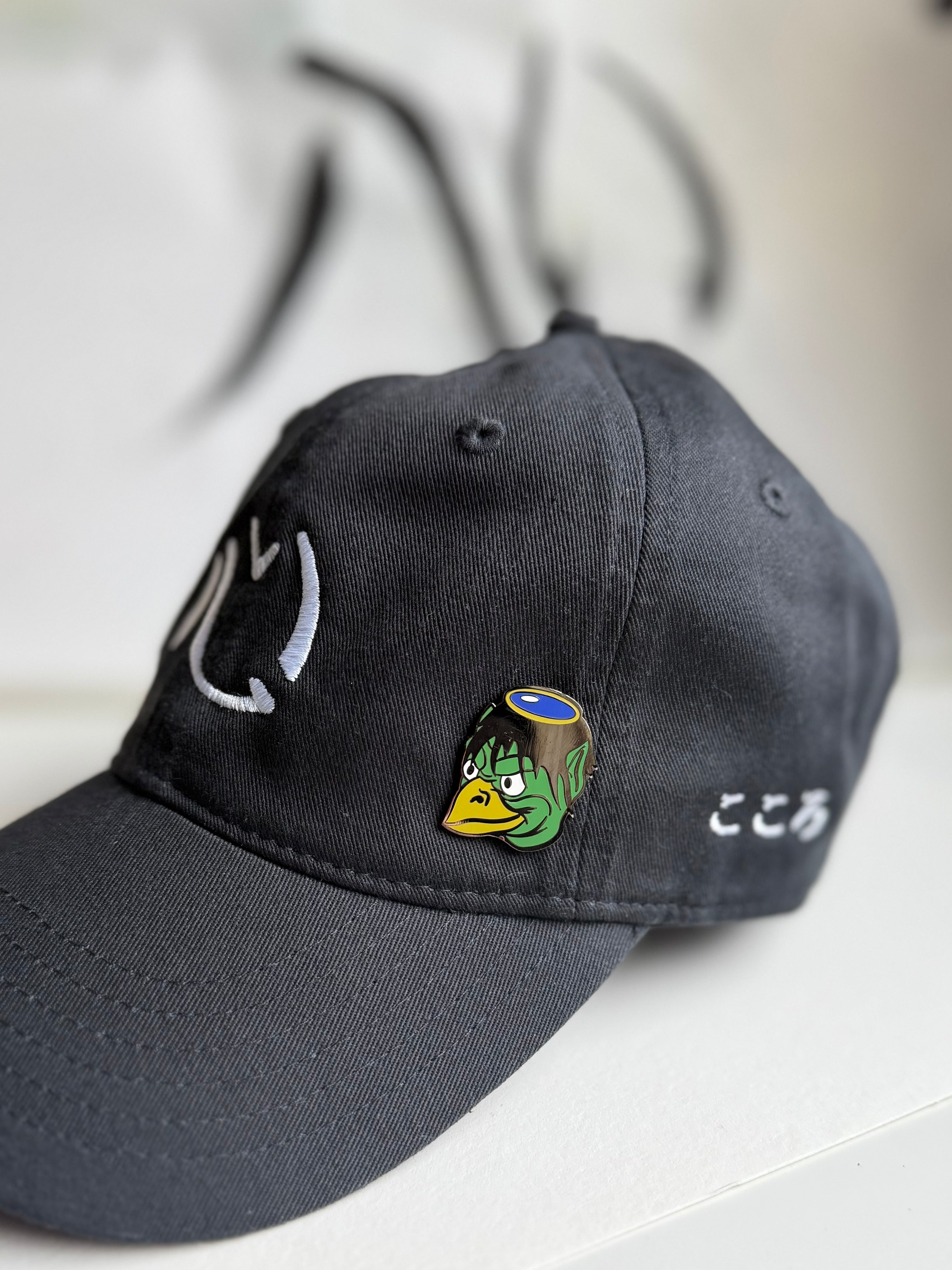Kappa enamel pin on an embroidered, black Kokoro hat with Kokoro calligraphy in the background